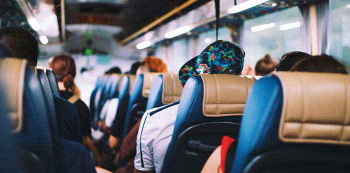 People seated on an airport shuttle bus, back view.